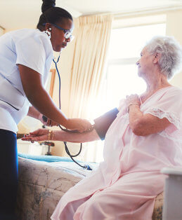 caregiver checking old woman's blood pressure